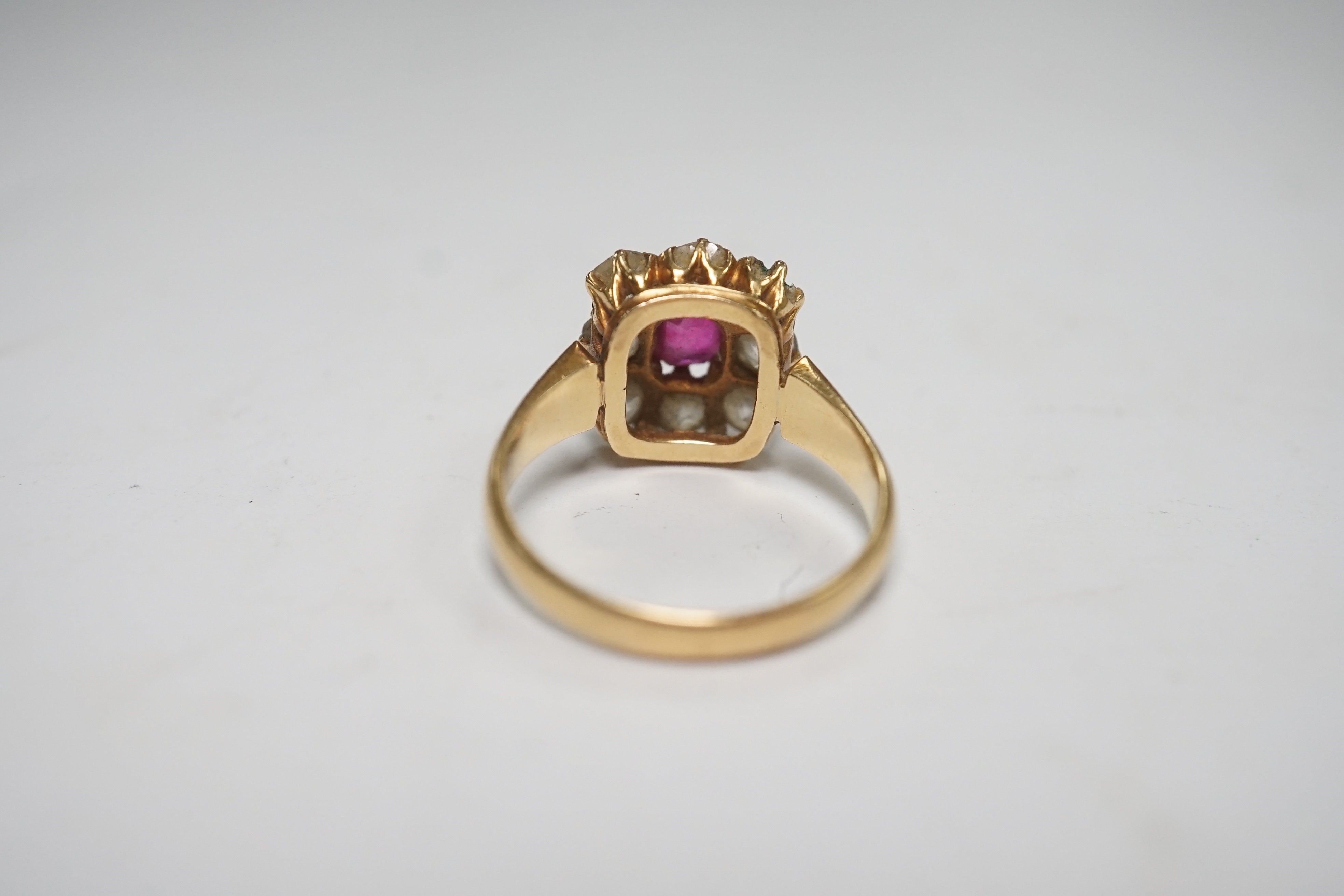 An early 20th century yellow metal, single stone ruby and eight stone diamond set square cluster ring, size O, gross weight 5 grams, one diamond missing. Condition - poor to fair